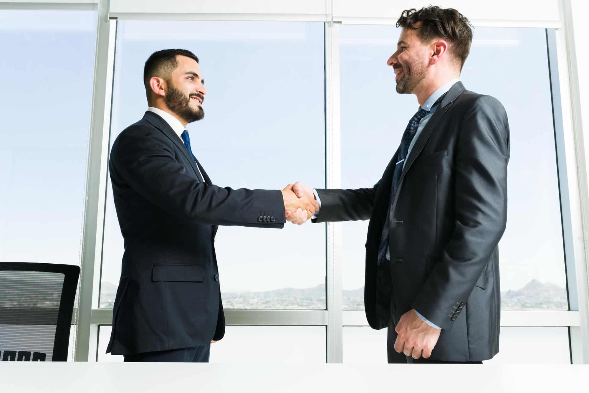 Two businessmen shake hands inside an office.