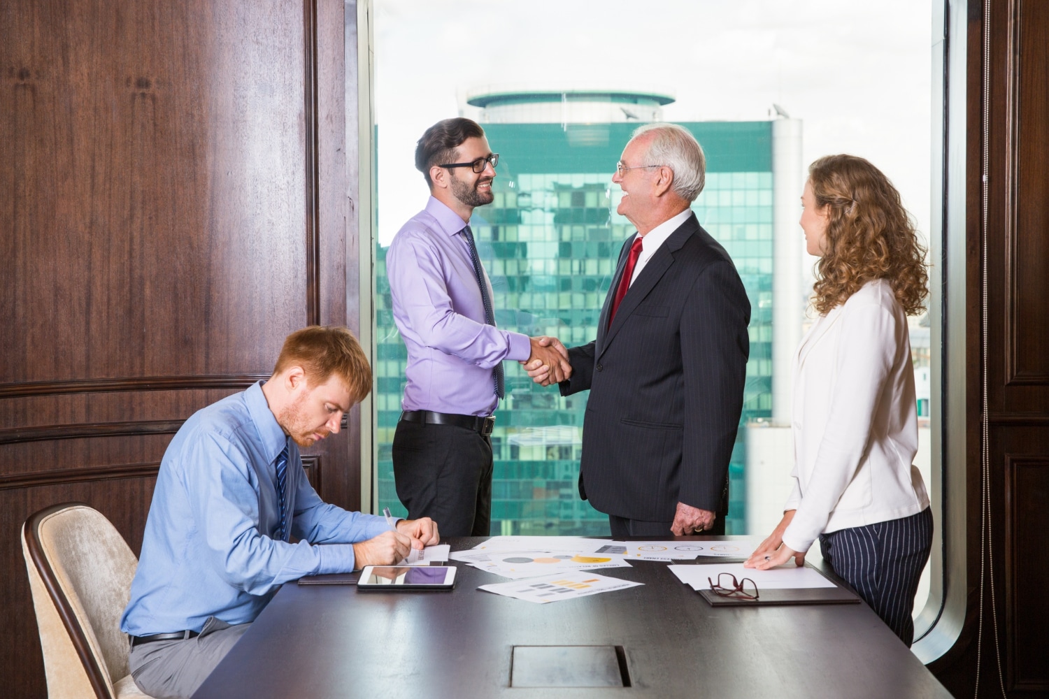 Two men shake hands, symbolizing a successful business agreement, while a woman observes with a smile.